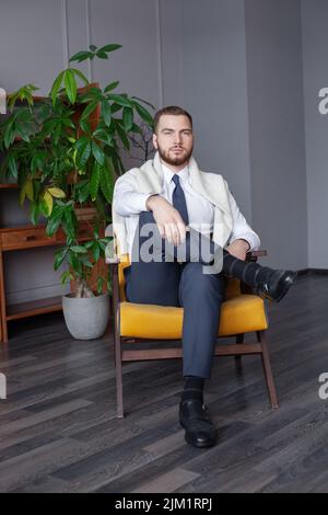 Junger, hübscher Mann mit Bart, Schnurrbart und trendiger Frisur, trägt Hemd und Pullover, hat ernsthaften Ausdruck Stockfoto