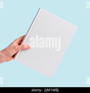 Hand hält Buch Mockup auf blauem Hintergrund. Weiße Deckelschablone. Literatur, Bildung, Lesekonzept. Hochwertige Fotos Stockfoto