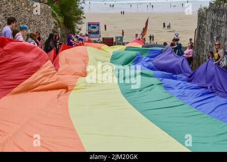 Das riesige farbenfrohe Cornwall ist stolz auf das Banner der Pride-Flagge, das von den Teilnehmern der Parade am Towan Beach Newquay in Großbritannien gehalten wird. Stockfoto