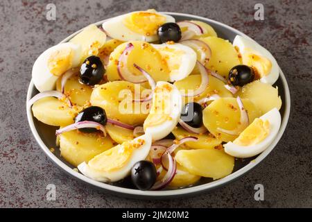 Orientalischer rumänischer Kartoffelsalat mit gekochten Eiern, Zwiebeln und Oliven, gewürzt mit Senfsauce aus nächster Nähe auf einem Teller auf dem Tisch. Horizontal Stockfoto