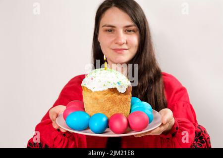 Eine Frau hält einen Osterkuchen und bemalte Eier auf weißem Hintergrund, Platz für Text kopieren. Stockfoto