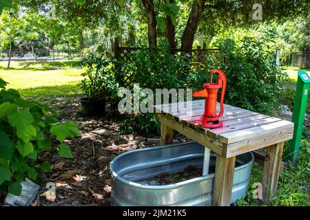 Antike alte rote Wasserpumpe auf einem Holztisch über einer silbernen Metallwanne in einem Garten. Gartengestaltung: Punta Gorda, Florida, History Park, Charlotte Stockfoto