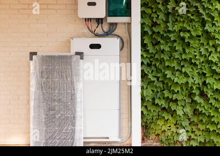 Elektrische Anlage für die Solaranlage mit Solarpanel, Batterie und Wechselrichter mit Vegetationspflanzen auf einer Seite Stockfoto