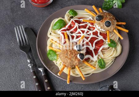 Koteletts sehen aus wie Spinnen mit Oliven und Trinkhalmen, serviert mit Spaghetti-Nudeln und Tomatensauce. Halloween-Frühstücksidee Stockfoto