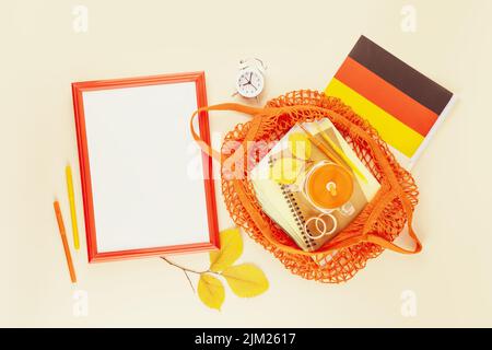 Zurück zur Schule in Deutschland. Schulbedarf in hellgelber Textiltasche, Rahmen und Deutschlandflagge auf hellem Hintergrund mit Herbstblättern und Kopie sp Stockfoto