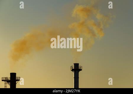 Goiania, Goiás, Brasilien – 04. August 2022: Rauch kommt aus zwei Schornsteinen einer Fabrik. Rauchverschmutzung durch die Fabrik mit dem Himmel im Hintergrund. Stockfoto
