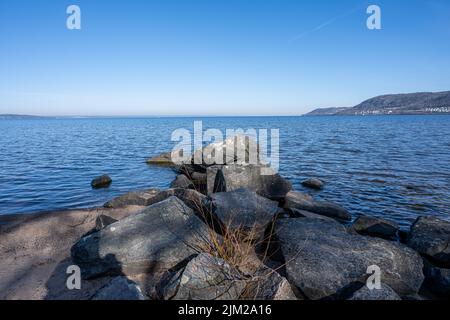 Felsbrocken als Teil eines Wellenbrechers in einem See. Bild vom See Vattern, Schweden. Blaues Wasser und Himmel im Hintergrund Stockfoto