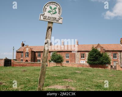 Das Manor of Brancaster und National Trust Schild auf dem Grün in Brancaster North Norfolk England UK Stockfoto