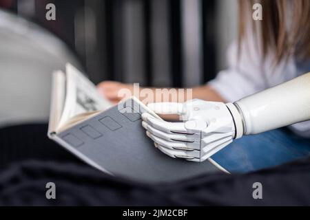 Motivierte Frau mit Behinderung Lernen mit prothetischen Arm, um Buch zu halten, während das Lesen, Mädchen führt ein normales Leben mit künstlichen Prothesen Extremität Stockfoto