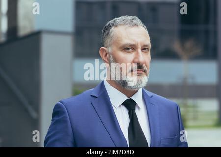 Nahaufnahme Porträt von grauhaarigen erfolgreichen Geschäftsmann Chef, Mann konzentriert und denken Blick auf die Kamera, Geschäftsmann Eigentümer im Anzug außerhalb des Büros Stockfoto