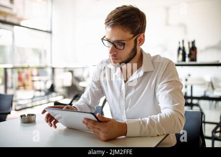 Junger Geschäftsmann, der Kaffee trinken und seine Arbeit im Café verrichten will. Menschen, Erfolg, Arbeitskonzept. Stockfoto