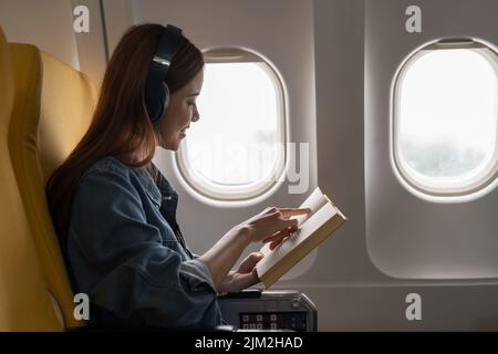 Schöne asiatische Reise Frau liest ein Buch im Flugzeug Stockfoto