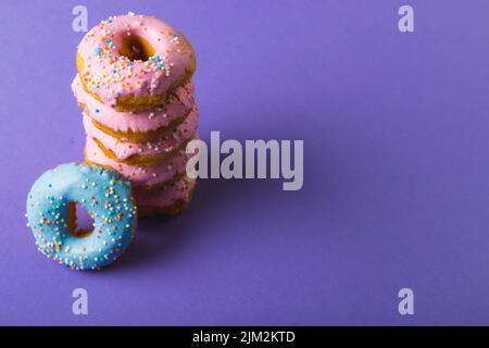 Große Ansicht von frischen Donuts mit Sprinklern durch einen Kopierraum vor violettem Hintergrund Stockfoto