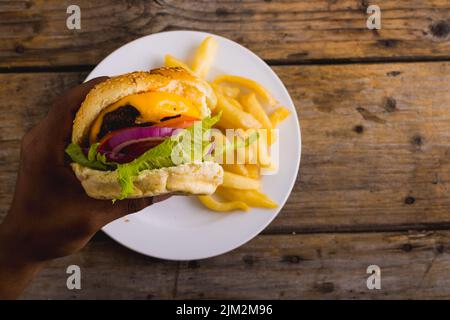 Hände eines afroamerikanischen Mannes, der Burger hat, während pommes auf dem Teller liegen, Platz kopieren Stockfoto