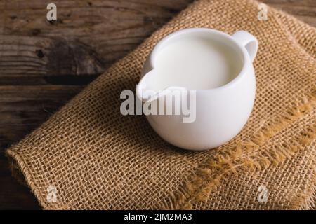 Milch im Krug auf Sackleinen am Holztisch, Platz kopieren Stockfoto