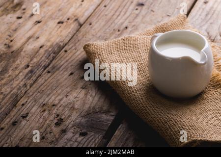 Milch im Krug mit Sackleinen auf Holztisch, Platz kopieren Stockfoto