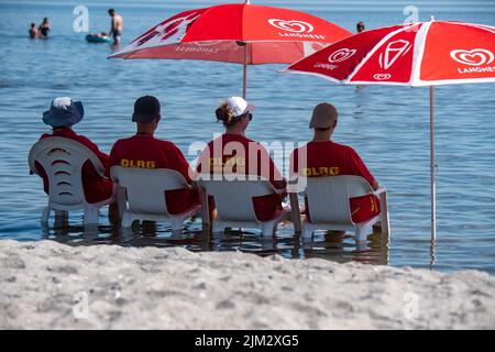Stralsund, Deutschland. 04. August 2022. Rettungsschwimmer der Deutschen Rettungsgesellschaft (DLRG) sitzen an diesem heißen Hochsommertag im kühlen Wasser des lido auf Stühlen und beobachten das Geschehen im Meer. Quelle: Stefan Sauer/dpa/Alamy Live News Stockfoto