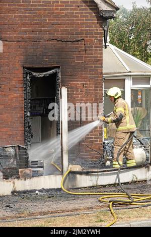 Hausbrand zwischen Holzbegrenzungszaun und Seitenwand Feuerwerkskreuz dämpfend Feuer unter Kontrolle gebracht verkohlte UPVC-Küchentürrahmen Essex England UK Stockfoto