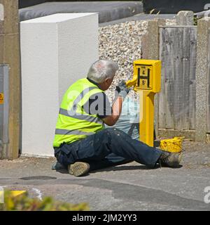 Arbeiter von Essex Fire and Rescue Service sitzt auf dem Bürgersteig mit Farbtopf Malerei gelben Straße Hydrant Schild trägt Sichtjacke UK Stockfoto