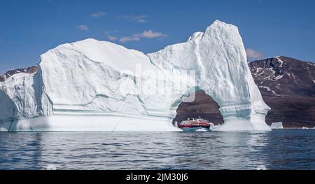 Hurtigrutes Expeditionskreuzfahrtschiff MS Fridtjof Nansen am 18. Juli 2022 durch einen Bogen in einem riesigen Eisberg in der Disko Bay, Grönland, gesehen Stockfoto