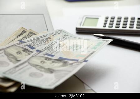 Hundert Dollar liegen auf einem Laptop auf dem Tisch und daneben ein Rechner und ein Stift, Wirtschaft und Finanzen Stockfoto