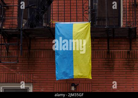 Eine ukrainische Flagge, die an einer Feuerflucht an der Seite eines roten Backsteingebäudes in New york hängt, zeigt Solidarität mit der Ukraine Stockfoto