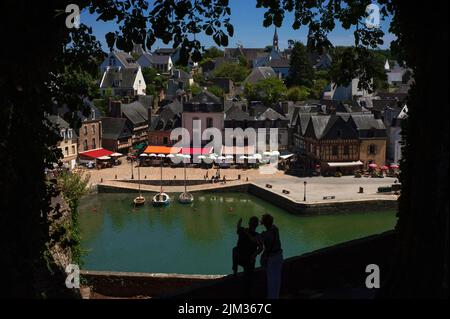 Ein Paar, das gegen den grünen Fluss Loch stand, schaute und zeigte nach unten auf den Place Saint-Sauveur im Saint-Goustan-Viertel von Auray, Morbihan, der südlichen Bretagne, Frankreich, gesäumt von Restaurants und Straßencafés mit bunten Markisen und Sonnenschirmen. Saint-Goustan, einst ein geschäftiges Fischerei- und Handelshafen, ist heute ein beliebtes Touristenziel, das einem Besuch des US-Gründervaters Benjamin Franklin im Jahr 1776 Tribut zollt. Stockfoto