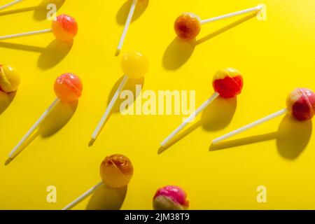 Nahaufnahme von über Kopf verstreuten Lutschern vor gelbem Hintergrund Stockfoto