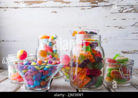 Nahaufnahme von bunten Süßigkeiten und Lutschern in Gläsern und Schüssel auf Holztisch Stockfoto