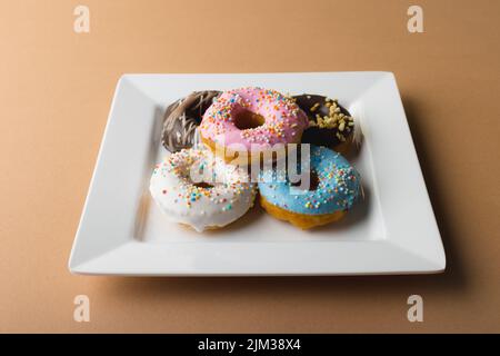 High-Angle-Ansicht von frischen Donuts in weißem Teller auf beigem Hintergrund Stockfoto