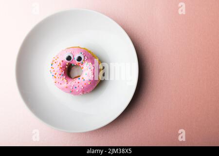 Direkt über Ansicht von frischem Donut mit schönen Augen in weißem Teller durch Kopierraum auf rosa Hintergrund Stockfoto