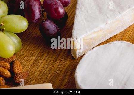 Nahaufnahme von verschiedenen Käsesorten mit Trauben und Mandeln auf Holzbrett, Kopierraum Stockfoto