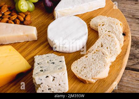 Nahaufnahme von verschiedenen Käsesorten mit Trauben und Mandeln auf Holzbrett, Kopierraum Stockfoto