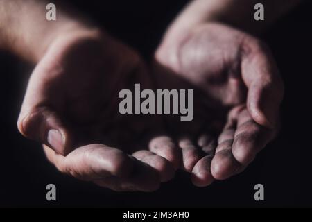 Schmutzige Hände eines hungernden armen Mannes auf dunklem Hintergrund. Hungriger Mann bittet auf schwarzem Hintergrund um Hilfe und Essen, Hände aus nächster Nähe. Stockfoto