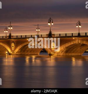 Langzeitbelichtung der Pont de Pierre über den Fluss Garonne in der Stadt Bordeaux, Frankreich, beleuchtet kurz nach Sonnenuntergang Stockfoto