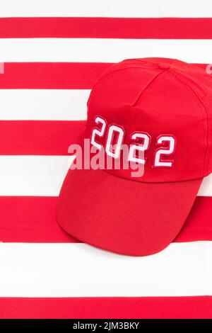 Red MAGA-Typ Hut mit 2022 Datum auf US Stars and Stripes Flagge. Für republikanische Siege bei den Mittelfristwahlen in den USA im November 2022 und der Roten Welle der US-Republikaner Stockfoto