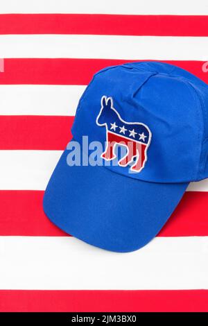 Blaue DNC-Kappe mit dem Esel-Emblem und US Stars and Stripes Flagge. Für die Präsidentschaftswahlen 2024 in den USA und die Vernichtung der Demokraten durch die republikanische Rote Welle. Stockfoto