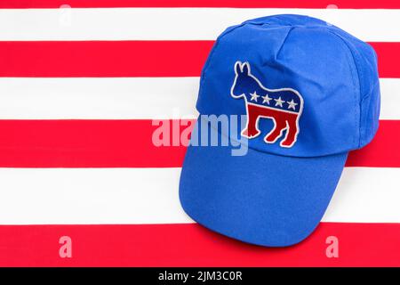 Blaue DNC-Kappe mit dem Esel-Emblem und US Stars and Stripes Flagge. Für die Präsidentschaftswahlen 2024 in den USA und die Vernichtung der Demokraten durch die republikanische Rote Welle. Stockfoto