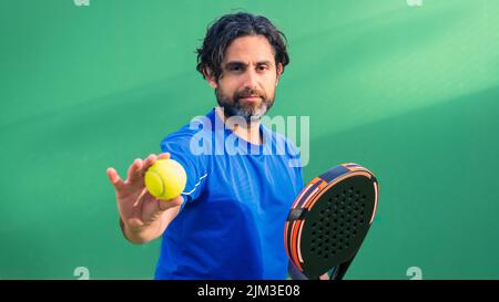 Monitor des Padels mit schwarzem Schläger und gelbem Tennisball in der Hand. Klasse für Studenten auf dem Tennisplatz im Freien. Mann Paddel Spieler spielt ein Spiel Stockfoto