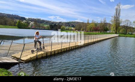 Nahaufnahme einer Frau, die Spaß hat und Elektroroller auf einer schwimmenden Brücke fährt Stockfoto