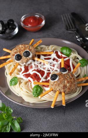 Koteletts sehen aus wie Spinnen mit Oliven und Trinkhalmen, serviert mit Spaghetti-Nudeln und Tomatensauce. Halloween Frühstück Idee, Vertikal-Format Stockfoto