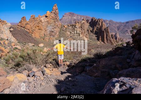Eine Rückaufnahme eines jungen Mannes auf dem Abstiegsweg in den Roques de Gracia und dem Roque Cinchado im Naturgebiet Teide auf Teneriffa, Kanarische Inseln Stockfoto