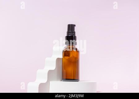 Bernsteinfarbene Glasflasche mit schwarzem Deckel auf einem Podium auf hellrosa Hintergrund. Hautpflegeprodukte, Naturkosmetik. Schönheitskonzept für Gesicht und Körper ca. Stockfoto