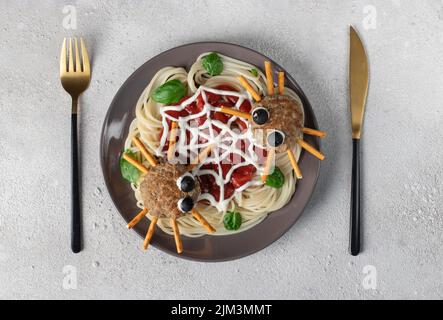 Koteletts sehen aus wie Spinnen mit Oliven und Trinkhalmen, serviert mit Spaghetti-Pasta und Tomatensauce auf hellgrauem Hintergrund. Halloween Frühstücksidee, Top Stockfoto