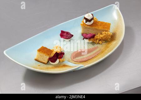 Weißer Teller mit gestylten süßen Biskuitkuchen, Feige und Eiscreme, goldenen Blättern und Blumen Stockfoto