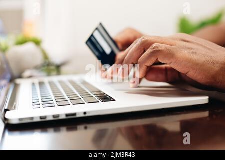Der Mann hält die Kreditkarte und benutzt einen Laptop. Online-Shopping Stockfoto