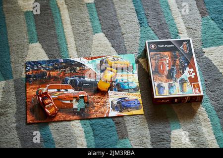 Die Mattel Cruz Ramirez und Lightning McQueen auf einem Trefl Disney Pixar Cars Puzzle neben Box. Stockfoto