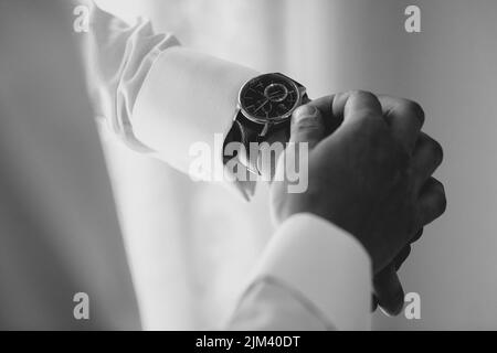 Eine Graustufenaufnahme der Hände eines Bräutigams, der seine Uhr am Hochzeitstag aufsetzt Stockfoto