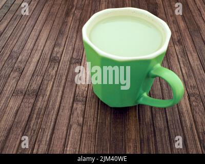 Nahaufnahme eines Matcha Latte aus Mandelmilch, in einem grünen Becher auf einem Holztisch Stockfoto