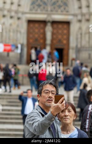Barcelona, Spanien - 21. März 2022: Japanische Touristen machen im Urlaub ein Selfie mit ihrem Handy vor dem Caterdal in Barcelona (Spanien). Stockfoto